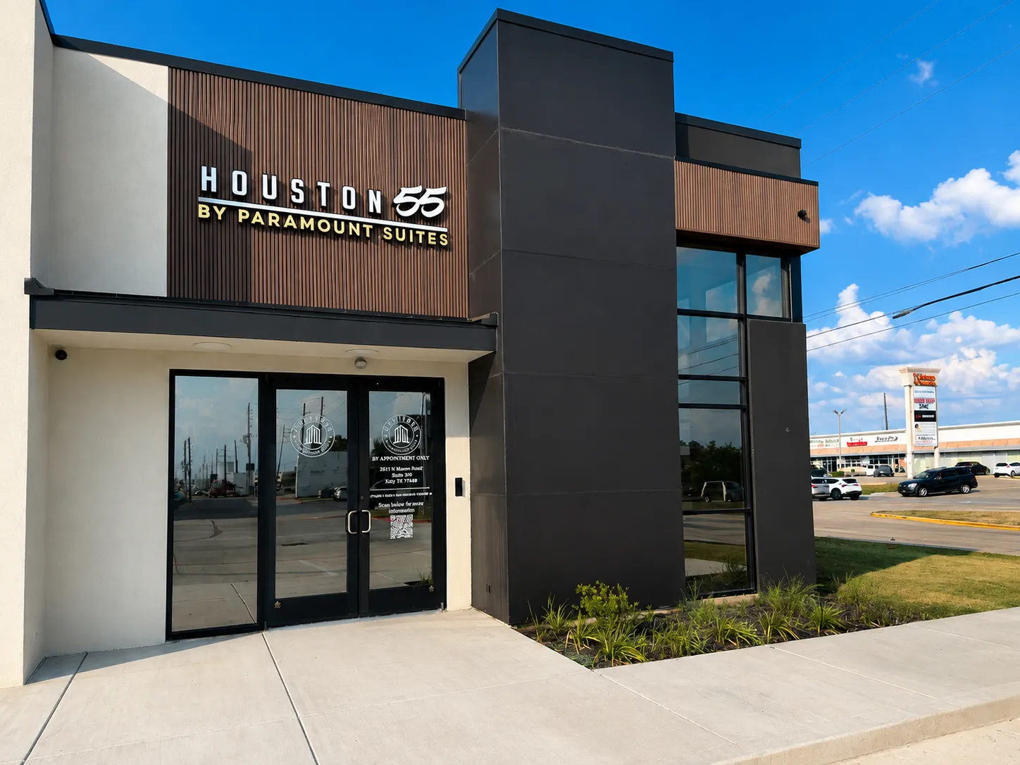 Exterior of Houston55 by Paramount Suites, featuring its glass entrance, wood-slat facade, and illuminated storefront sign.